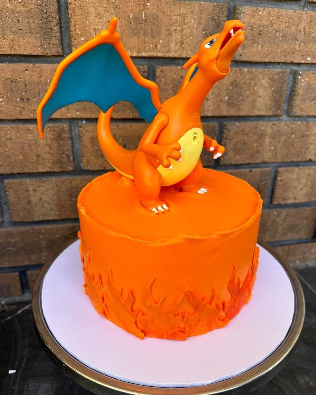 Orange Charizard Pokemon birthday cake with orange fondant flames around base and Charizard figurine topper with blue wings